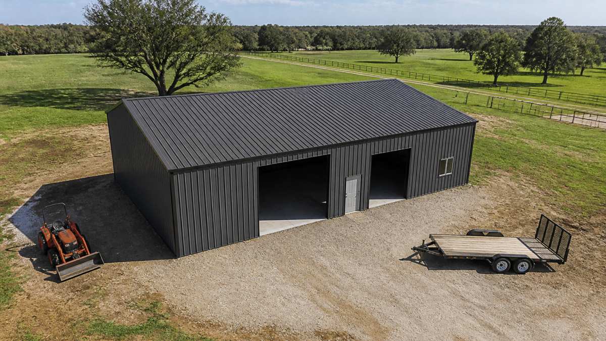 Aerial view of a newly installed metal building on a rural property with clear skies, showing the structure's full footprint and surrounding landscape with equipment nearby